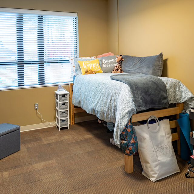 Interior of Pat Barker Hall including a twin bed with a number of storage carts for staying organized.