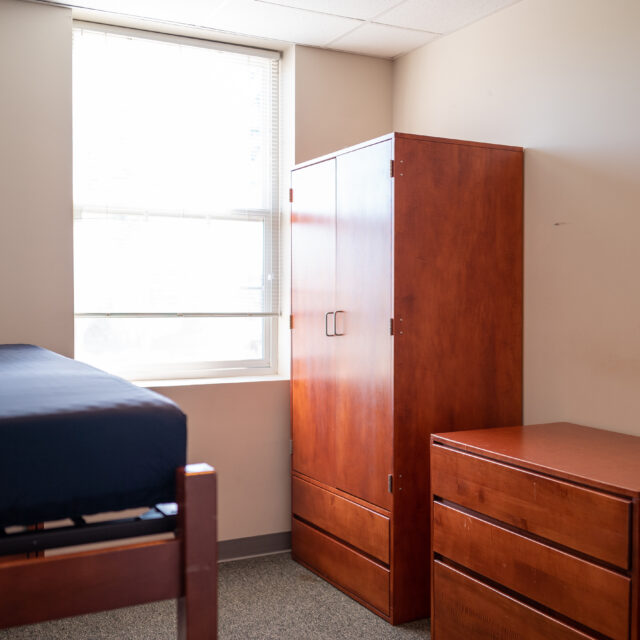 Image of an empty room including a twin bed and wardrobe inside Bob Barker Hall.