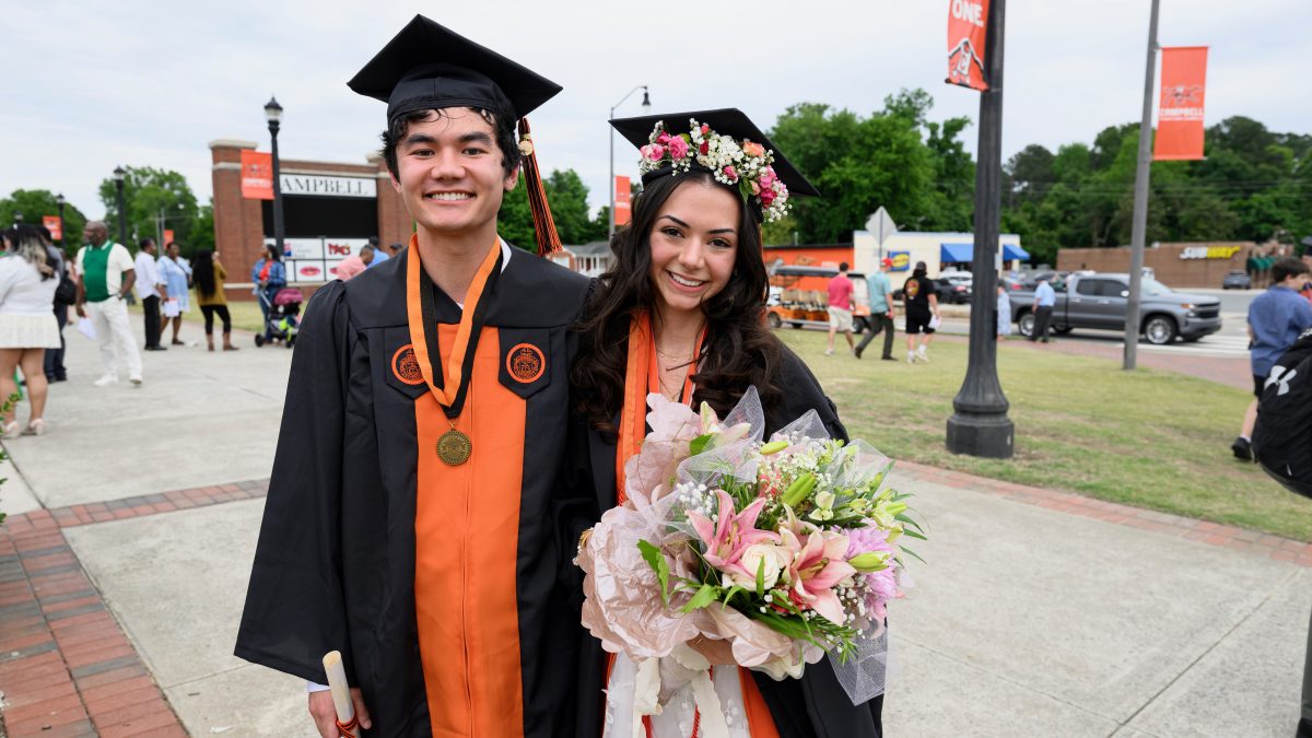 Two Campbell graduates posing for picture. One is holding flowers.