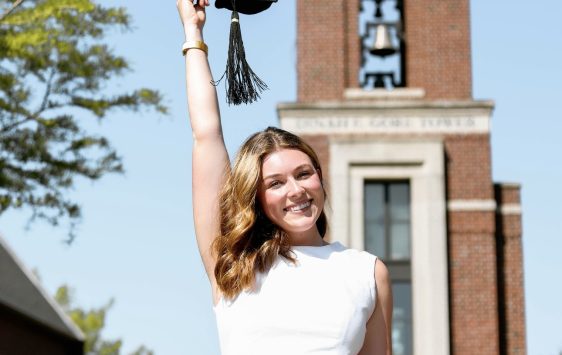 Sydney Higgins, student posing with graduation cap in front of bell tower