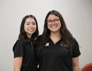 Two female pharmacy students wearing black polos with CPHS logo
