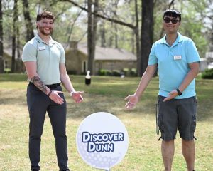 two male students on a golf course point to a golf ball sign