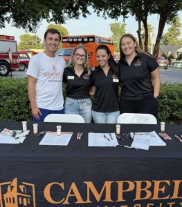Four students standing behind a folding table smiling