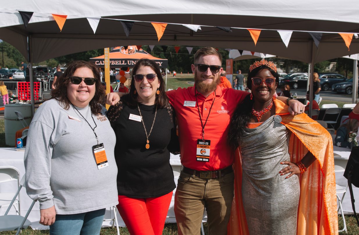 Four Campbell alumni standing together, smiling and posing for a photo