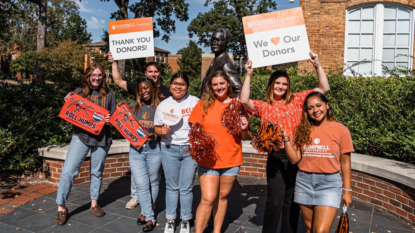 Students with giving day signs around the statue of JA Campbell