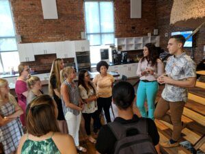 Side view of students gathered around Tom Jacobs in the brick-and-hardwood of the HQ Raleigh space. 