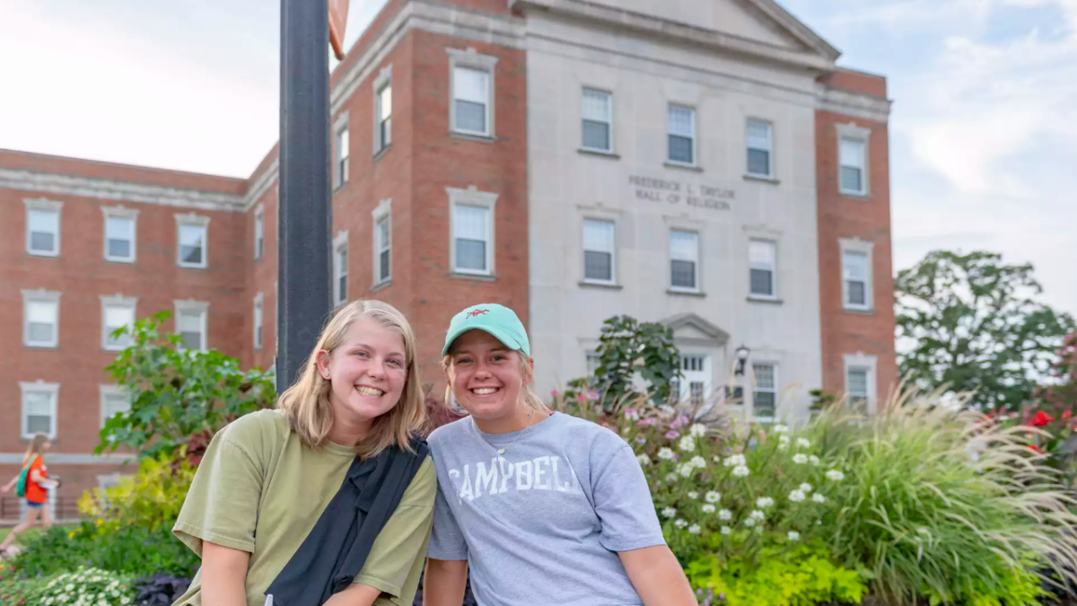 two blond-haired girls smile at camera, seated on a bench in front of Butler Chapel