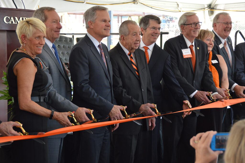 Dr. Creed, Bernard McLeod, and other trustees stand in a line with their scissors poised to cut an orange ribbon at the ceremony. 