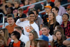 smiling male student in football stands gives two peace signs.