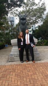 Photo of Vis competitors, a woman and man, standing in front of a dragon statue in Hong Kong.