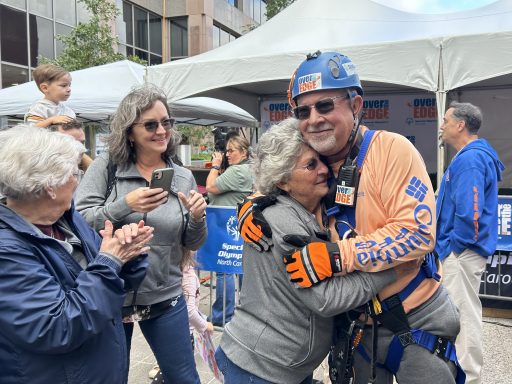 Photo of Professor Jon Powell '98 hugging his 90-year-old mother after going over the edge of the Wells Fargo Building for Special Olympics