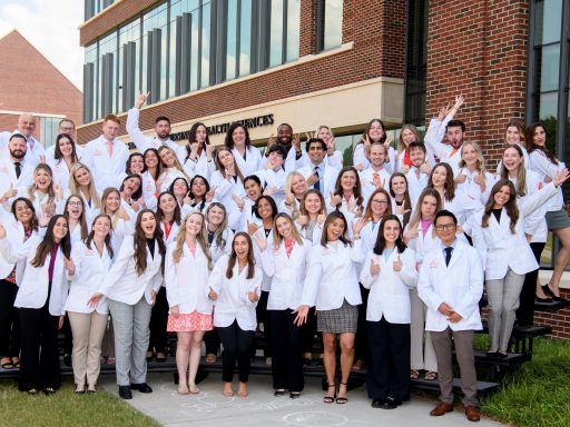 Group photo of PA Class of 2026 wearing short white coats on risers in front of Smith Hall