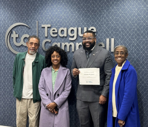 Photo of some of Charlotte W. Clark's family members with Campbell Law Student Clinton Jones '28 holding a certificate in front of a Teague Campbell sign.
