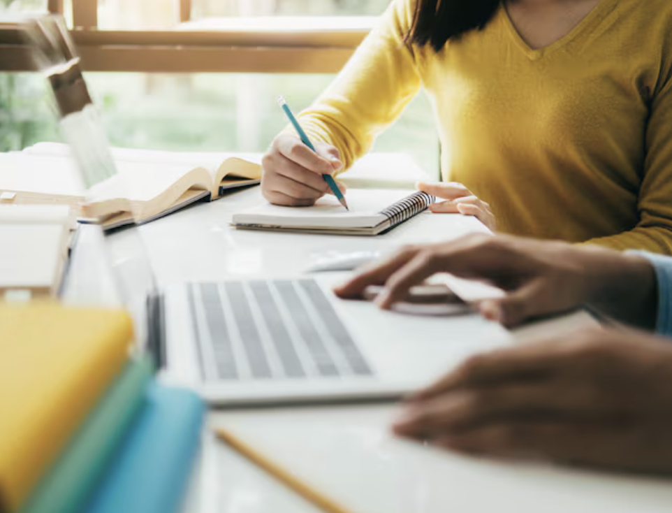 Photo of hands on a laptop and a woman writing in a notebook