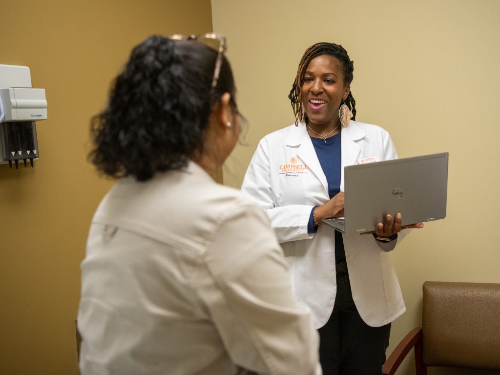 Pharmacy student holding laptop while talking with a patient at doctor's office