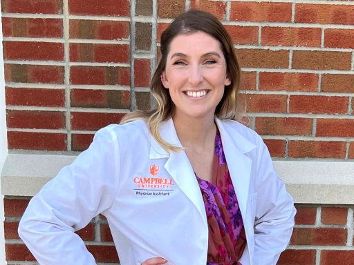 Alyssa Price wearing her student white coat with her hands on her hips in front of a brick wall.