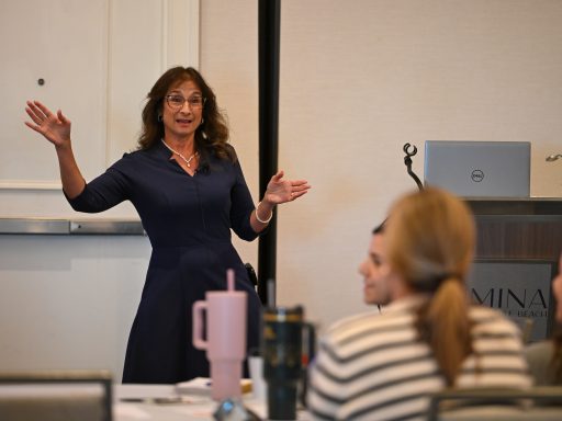 Presenter in blue dress holds arms out while talking.