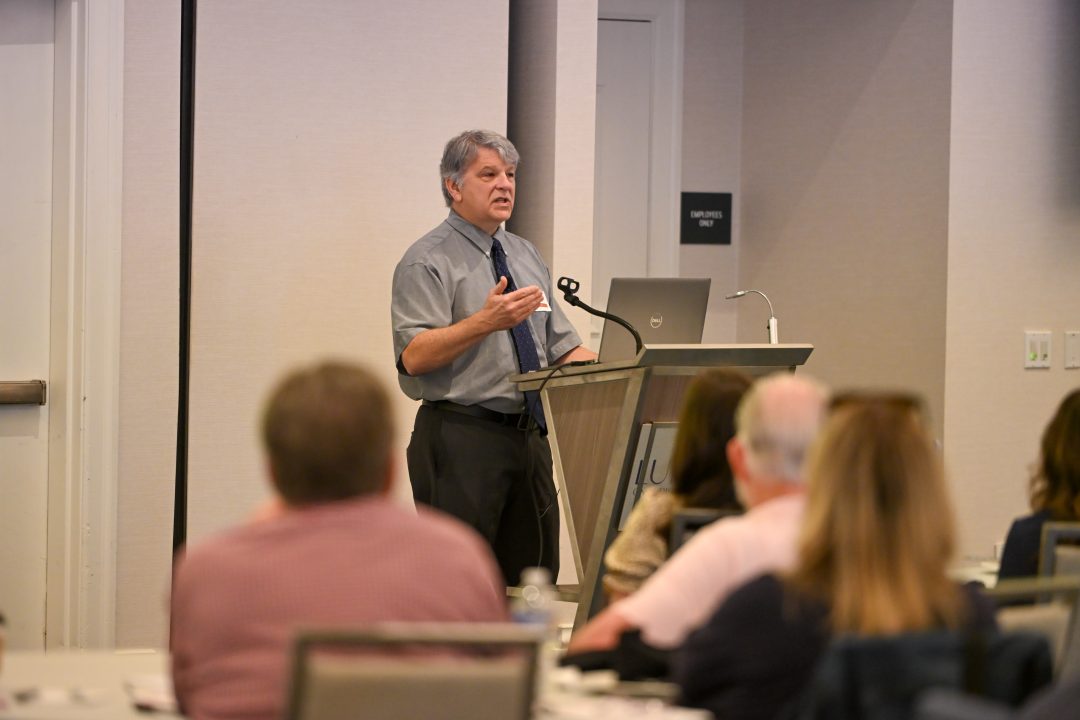 Speaker gesturing to attendees from podium.