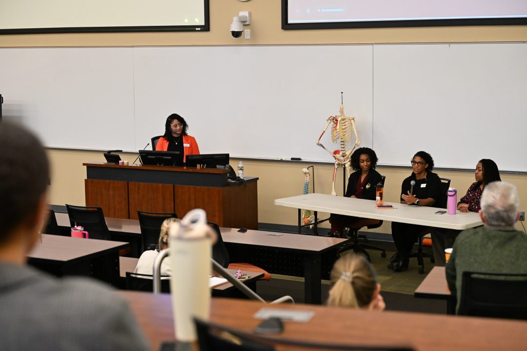 Three person female panel at front of room with female student at the podium