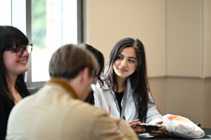 Student with long dark hair looks over at a group of people talking.