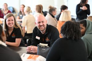 Dr. Brad Myers smiles at a guest while sitting around a therapy table talking with participants.
