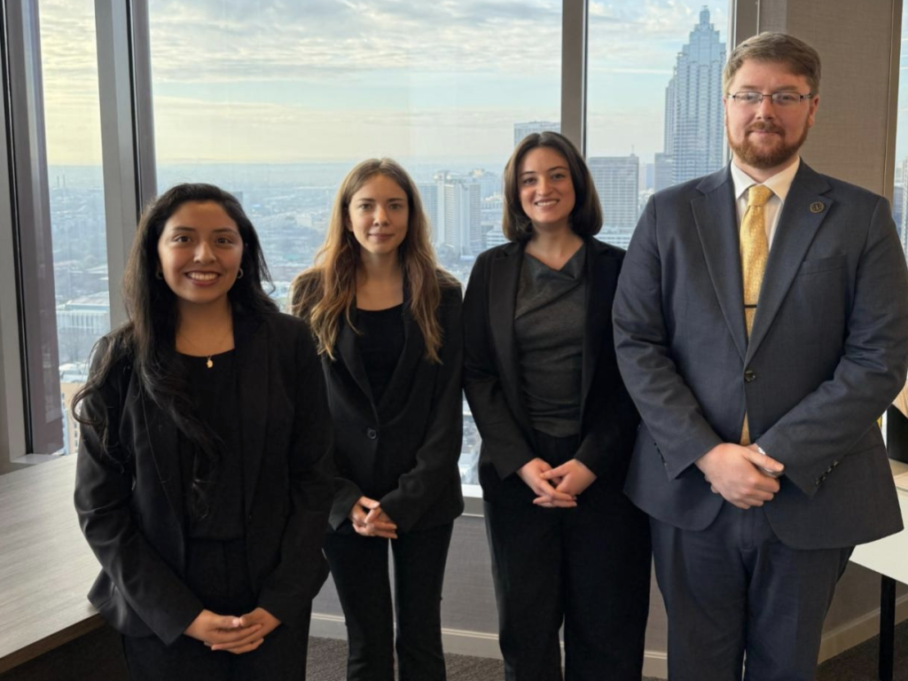 Photo of four student advocates posing in suits with Atlanta skyline in background