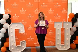 Incoming pharmacy students stands in front of a large orange backdrop smiling for a photo.