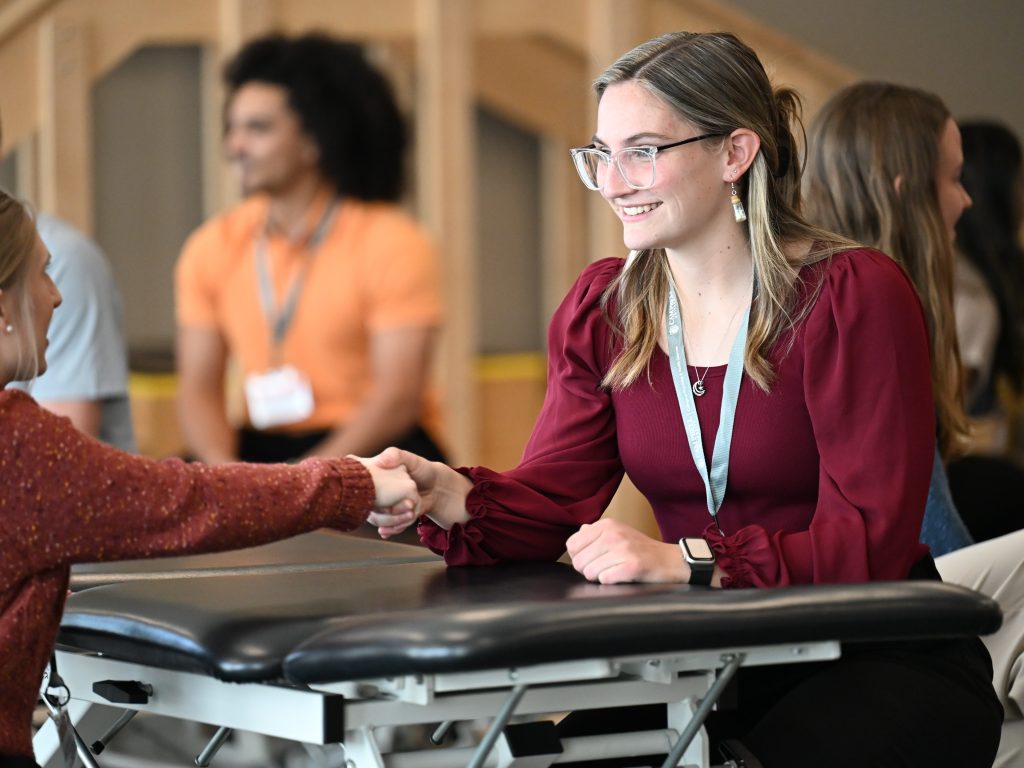 Two female students shake hands while sitting across a therapy table.