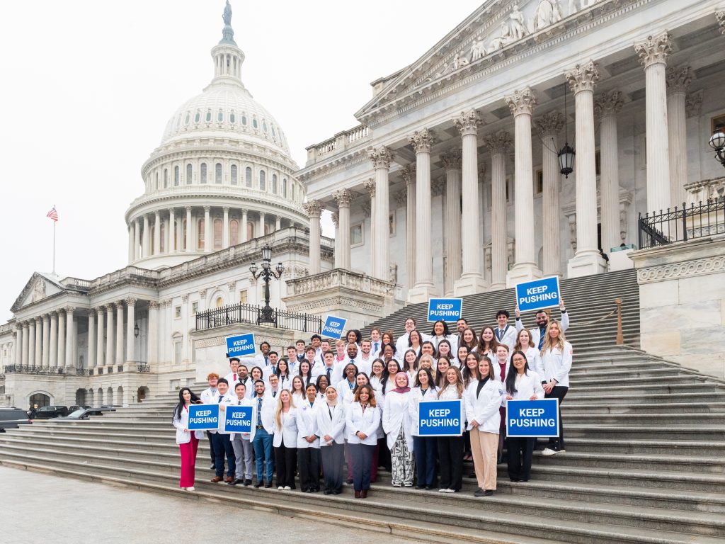 A group of about 50 pharmacy students wearing white coats holding signs with 