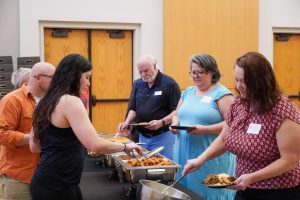 A group of five people go through a buffet line serving themselves food.