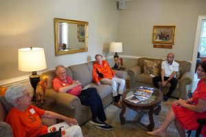 A group of five individuals sitting on couches and chairs. 