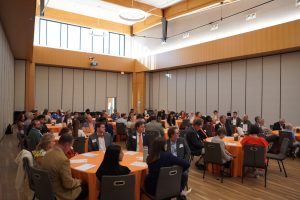 A large ballroom with several tables filled with people in suits and dresses.