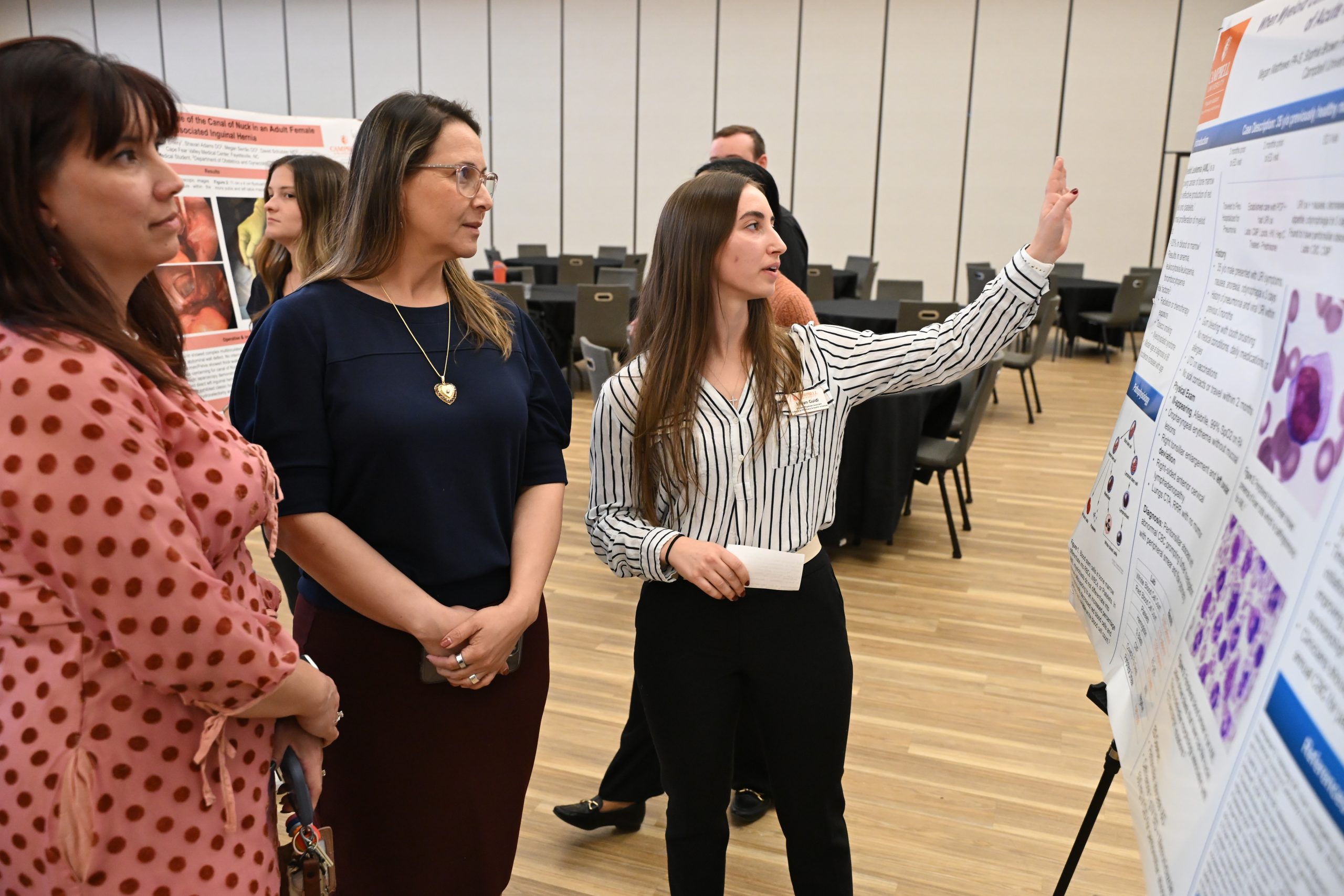 Female student pointing to poster with two female faculty members listening to her