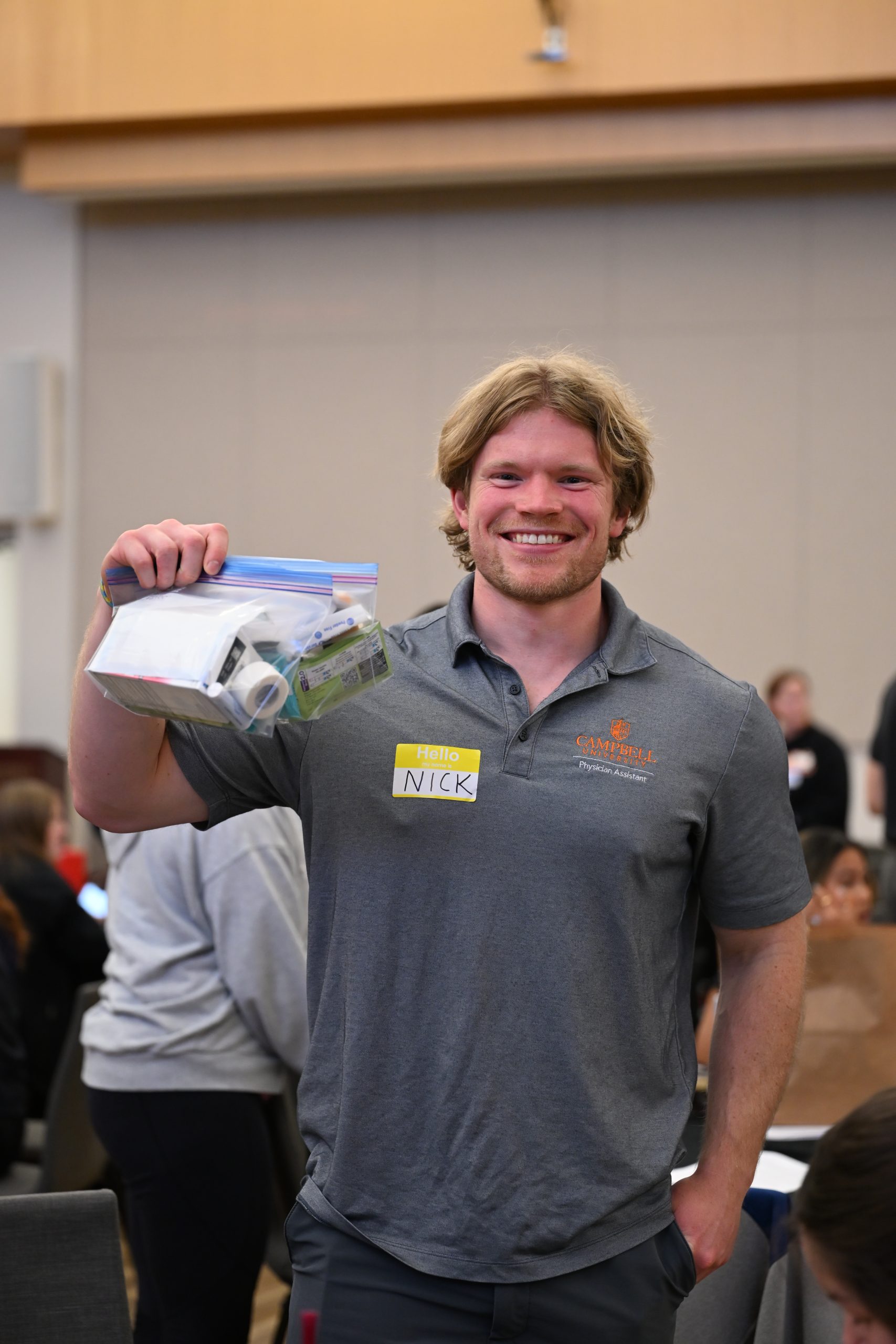 PA student wearing grey polo shirt holding a Hope Kit in a plastic bag