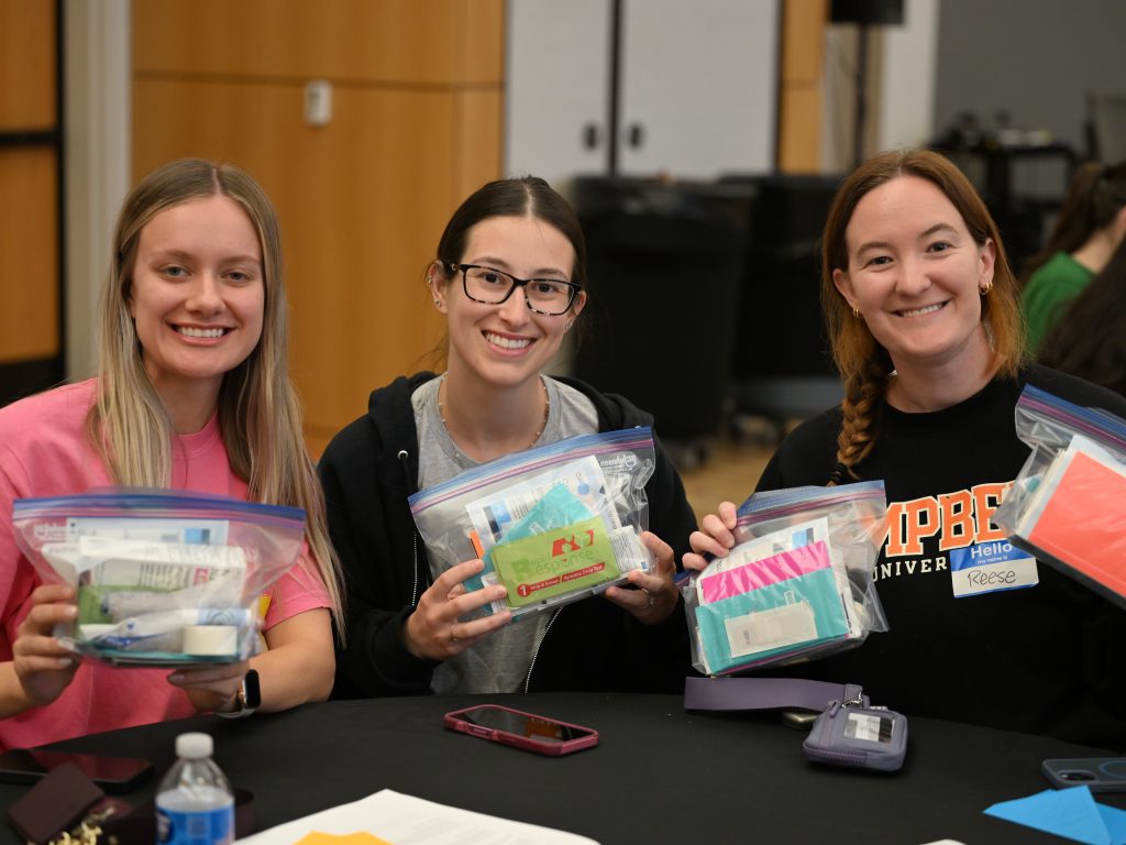 Three female students sitting at a table holding Hope Kits