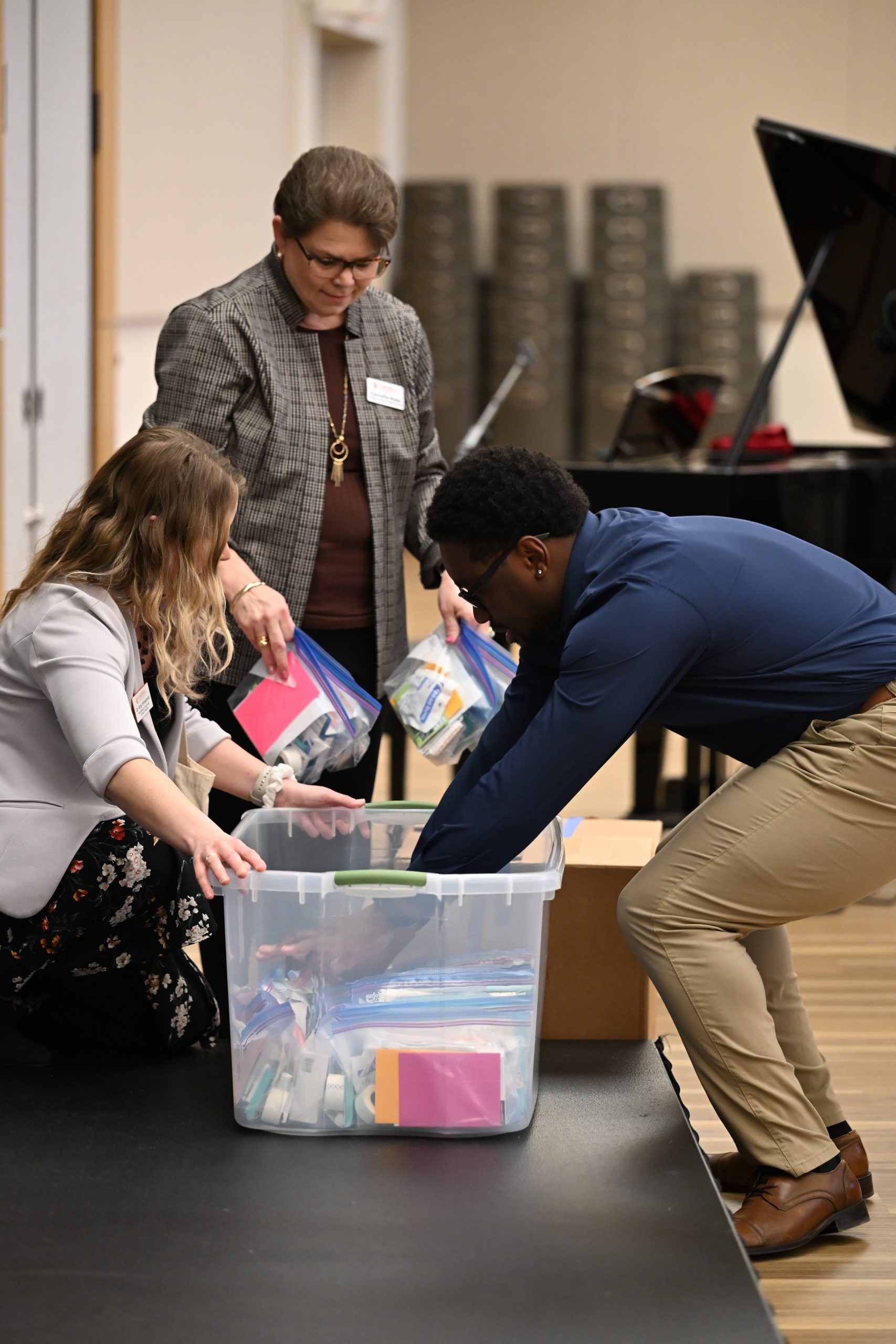 Student placing Hope Kits in plastic bin with two ladies looking on