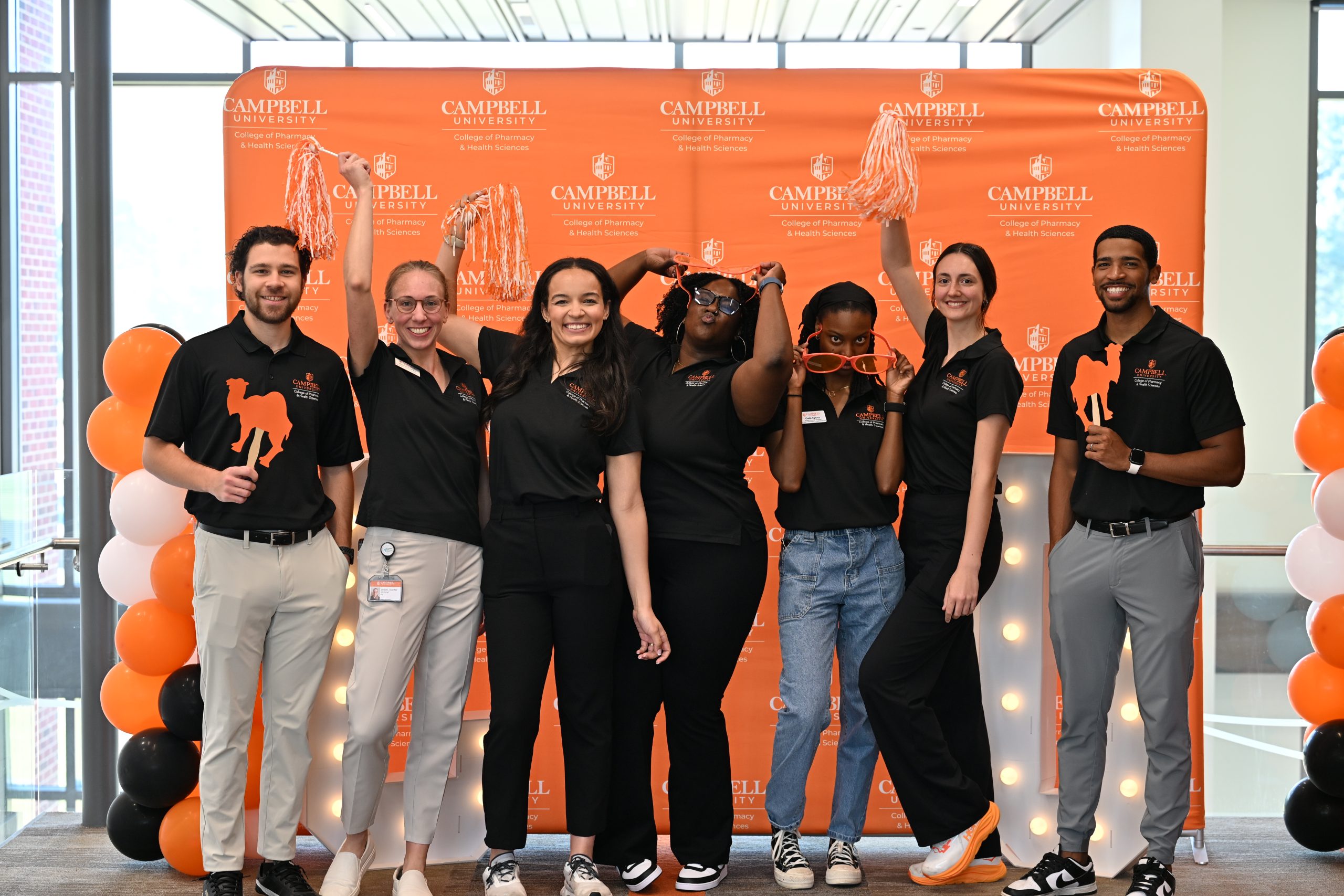 Male and female students wearing black polo shirts holding pom-poms with big smiles.