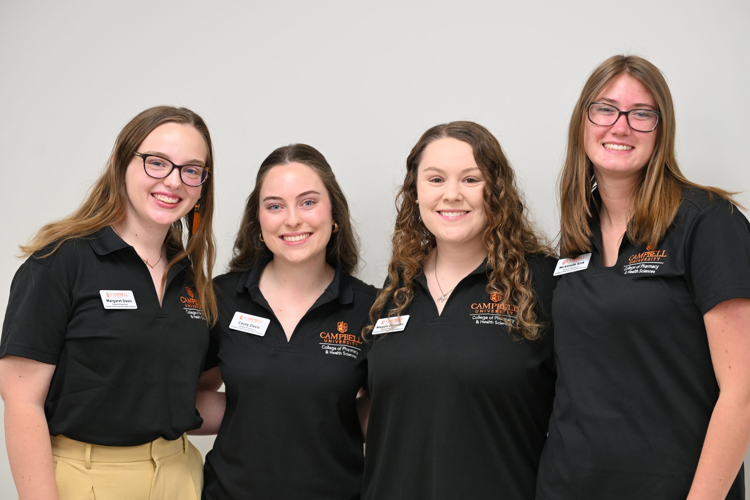 Group of female pharmacy students wearing black polo shirts smiling at camera.