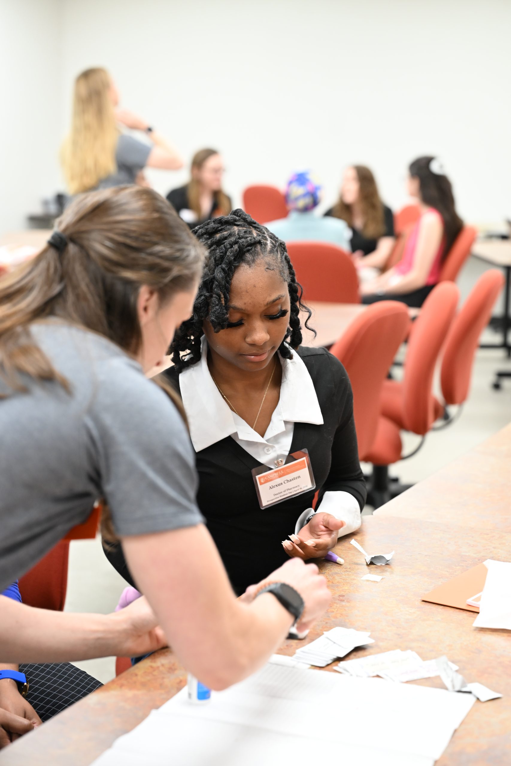 Female professor in grey shirt helping a prospective student prick her finger for a glucose test activity.
