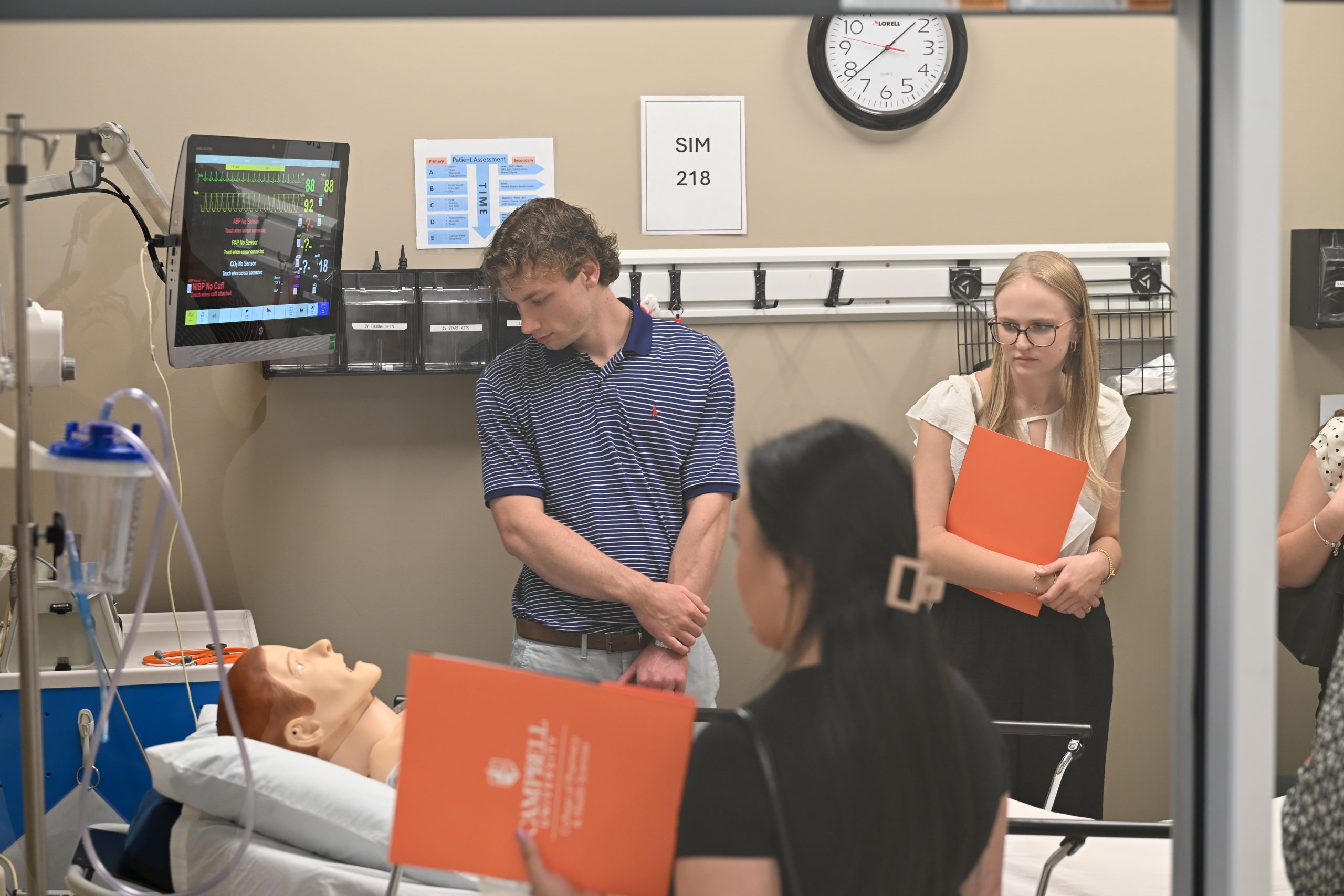 male and female prospective students in simulation lab looking at simulation mannequin and equipment.