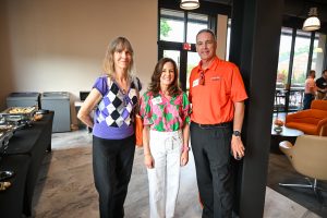 Three individuals pose for a photo, smiling. One is wearing a Campbell University orange polo. 