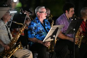 Three individuals appear to be playing saxophones at night with sheet music on stands in front of them.