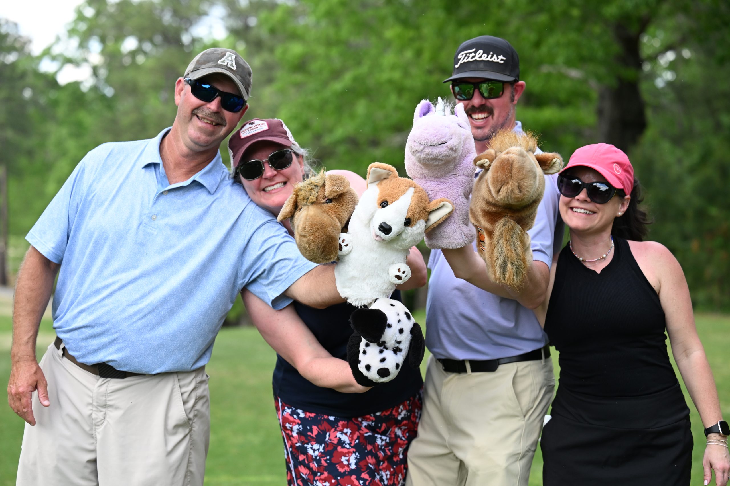 Two male and two female golfers wearing hats and sunglasses holding golf club covers