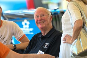 An individual smiles and looks up. They are surrounded by other people, out of focus from the rest of the image.