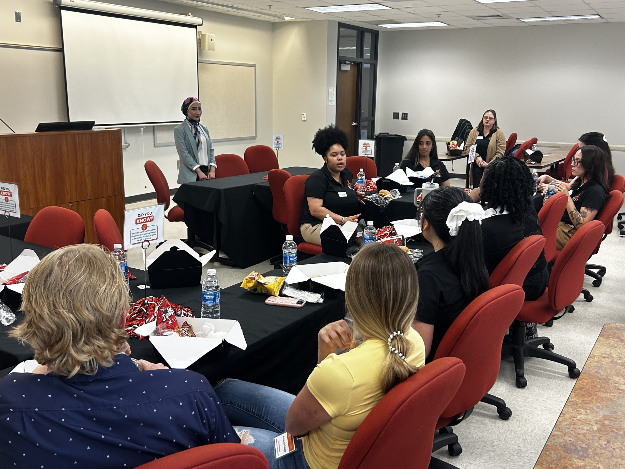 Group of female and male students, prospective students, guests, faculty and staff eating lunch together.