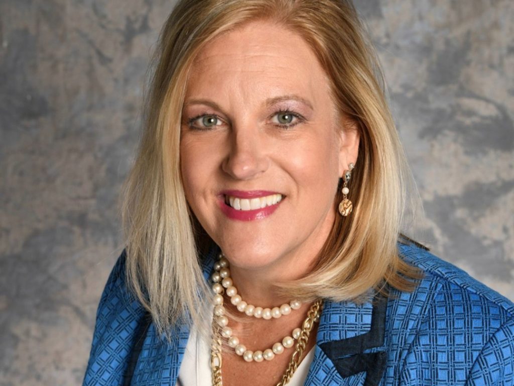 Female wearing white shirt and blue blazer with gold necklaces