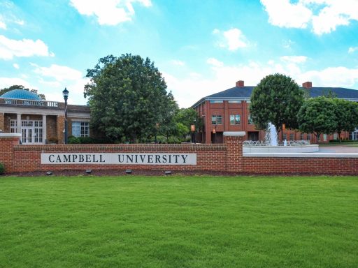 Campbell University sign in brick and concrete with a fountain behind it and with Carrie Rich Hall and Maddox Hall in the background