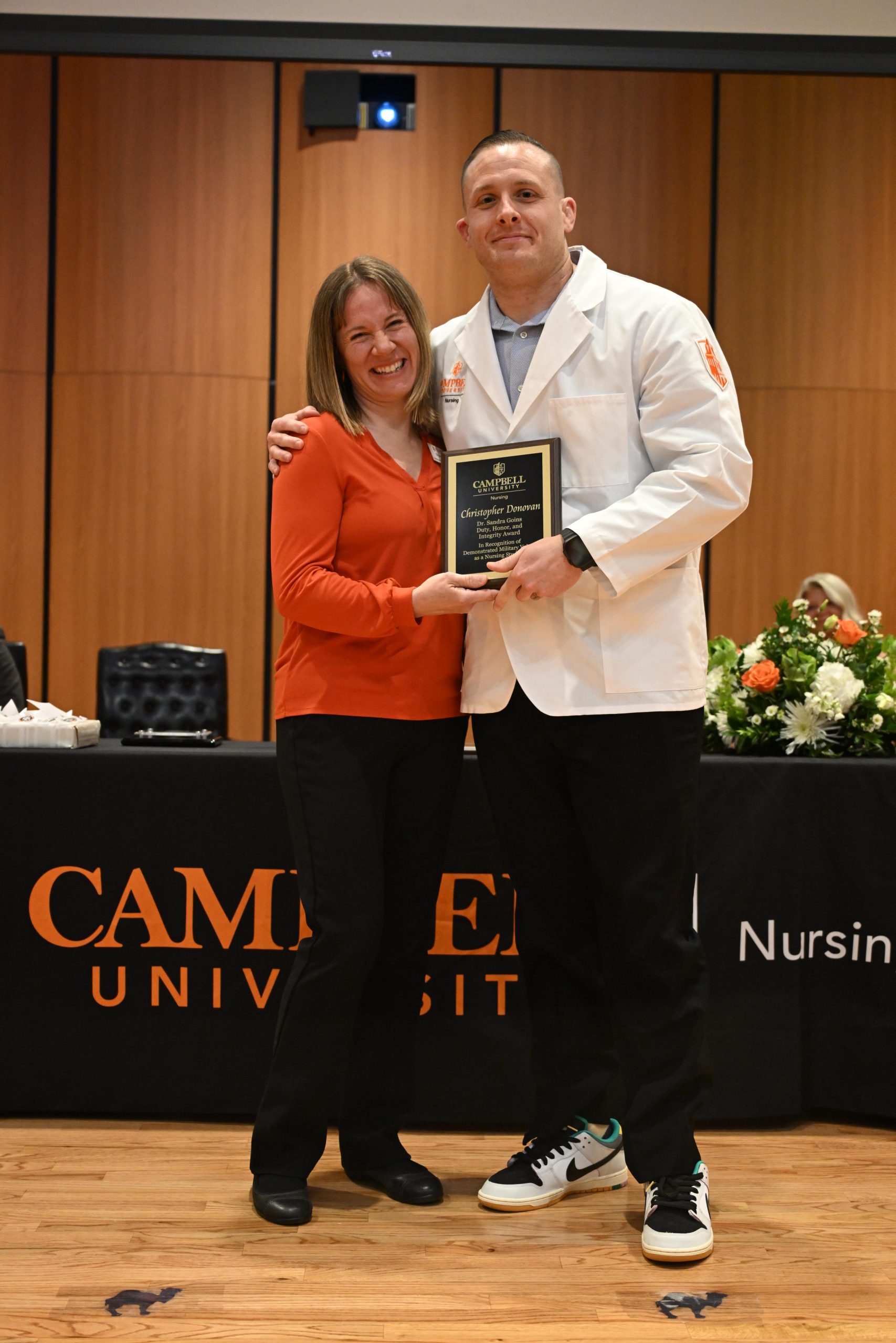 Female faculty member stands with male student holding plaque.