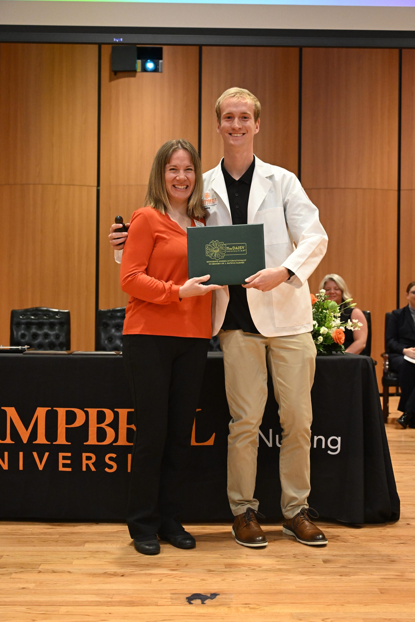 Female faculty member standing with male student holding plaque.