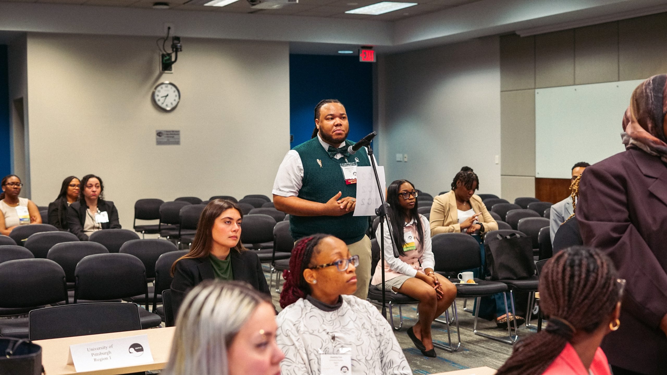 Male student standing at microphone waiting to speak.
